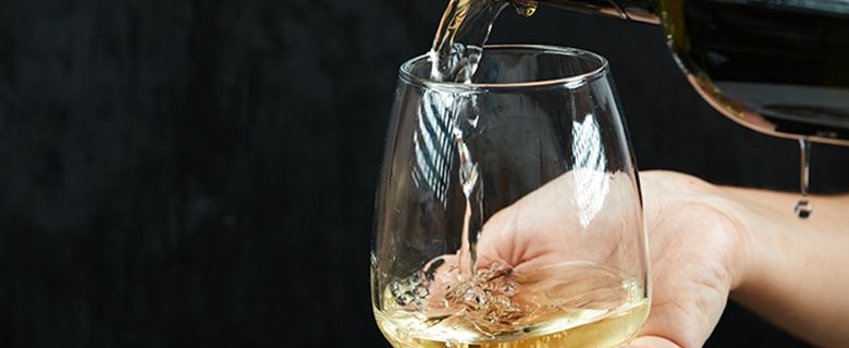 Pouring white wine into the wine glass on dark background