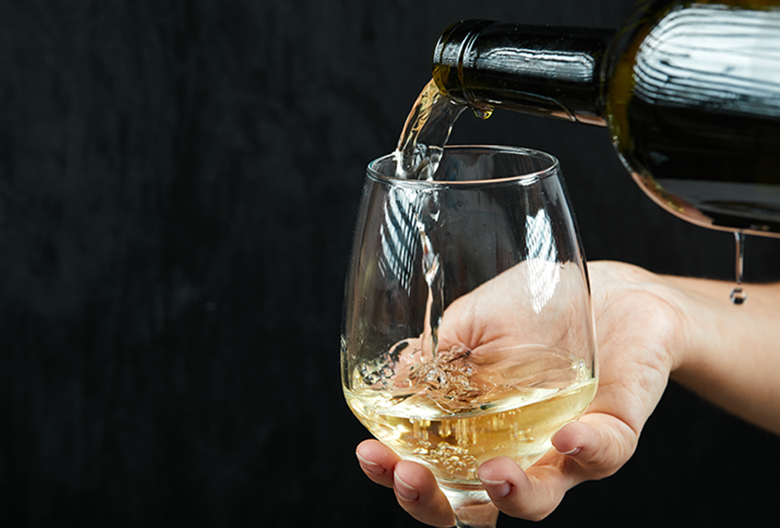 Pouring white wine into the wine glass on dark background