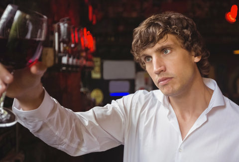 Bartender looking at glass of red wine at bar counter